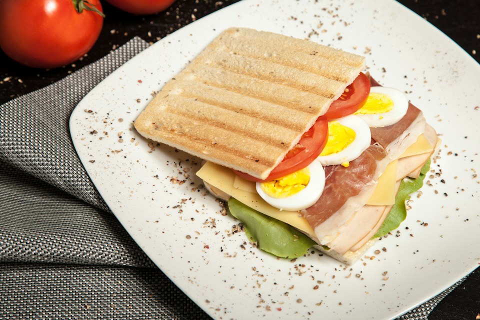 Sfeerfoto van een sandwich met ei, tomaat en kaas op een bord